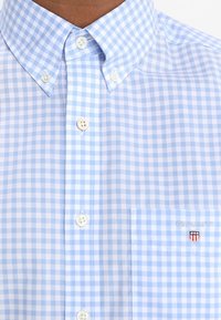 Camicia a quadri azzurro chiaro e bianco con colletto button-down, bottoni bianchi e taschino sul petto con logo ricamato.
