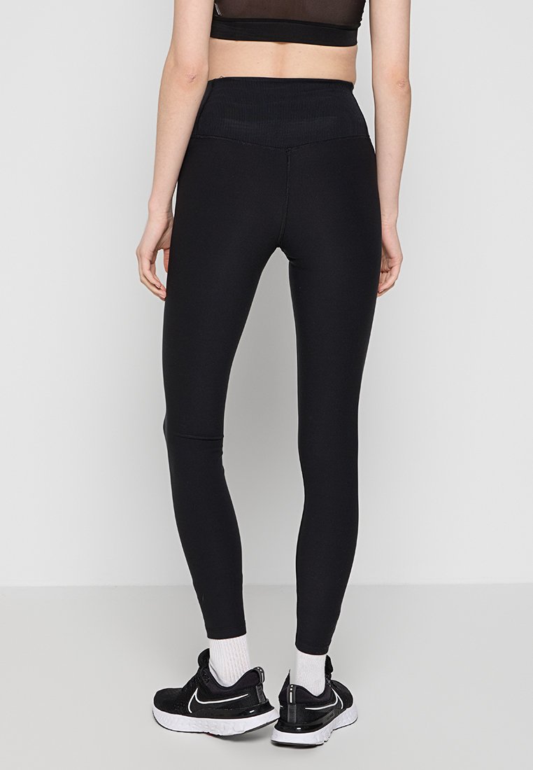 Leggings neri a vita alta realizzati in materiale elasticizzato, con una cintura a coste. Indossati con sneaker nere e calzini bianchi.