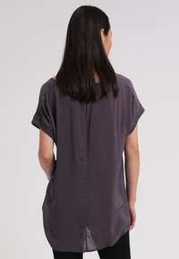 Afslappet pasform, kortærmet top i mørkegrå stof. Glat tekstur med en rund kant og en midtersøm detalje på bagsiden.