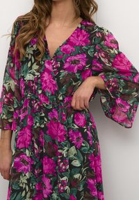 Blumenkleid mit langen, schwingenden Ärmeln, das lebendige rosa und grüne Blumen auf schwarzem Hintergrund zeigt. Elastischer Taillenbund und V-Ausschnitt-Design.