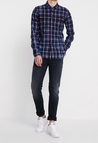 Granatowa w kratę koszula z białymi i czerwonymi akcentami, fason z guzikami, długie rękawy i dwie kieszenie na piersi; zestawiona z ciemnymi dżinsami i białymi trampkami.