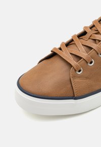 Brown leather sneaker featuring a smooth texture, round toe, and contrasting white rubber sole. Includes brown laces and metal eyelets.