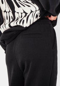 Zwarte joggingsbroek met een relaxte pasvorm, voorzien van een achterzakdetail en een elastische tailleband voor comfort. De stof lijkt soepel.