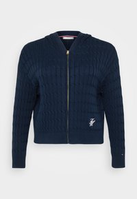 Σκούρο μπλε πλεκτή κουκούλα με υφή καλωδίου, χρυσό φερμουάρ, ριμπ μανίκια και στρίφωμα, με μικρό κεντημένο λογότυπο στο στήθος.