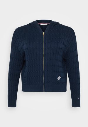 Merihenkinen neulehuppari, jossa on teksturoitu letkukuvio, kultainen vetoketju, ribbikaulus ja helma, sekä pieni brodeerattu logo rinnassa.