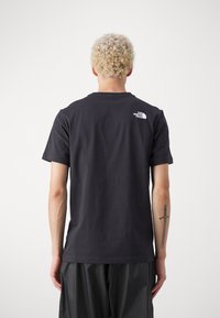 Zwart katoenen T-shirt met een klassieke pasvorm, voorzien van een klein wit logo op de achterkant. Korte mouwen en een ronde hals.