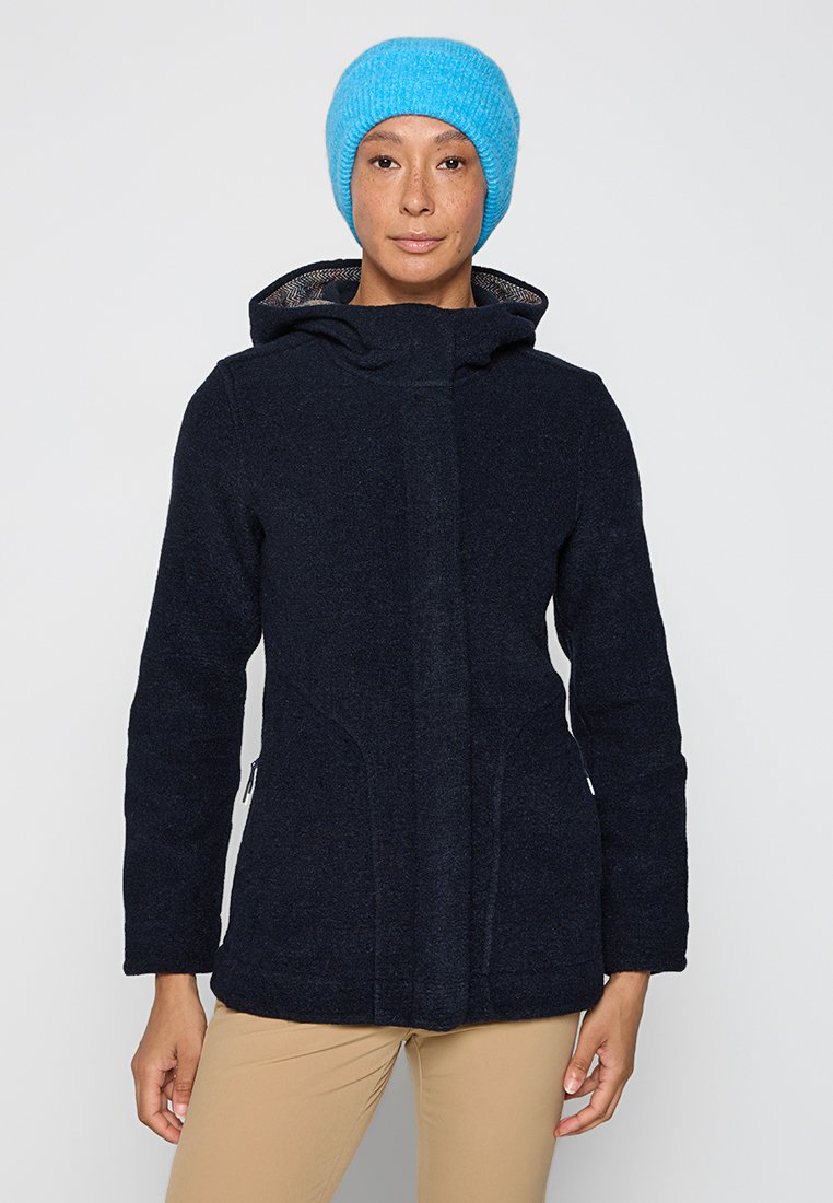 Marineblaues Wollmischjackett mit Kapuze, ausgestattet mit Reißverschluss-Seitentaschen und nahtlosem Vorderdesign. Kombiniert mit einer leuchtend blauen Strickmütze.