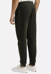 Ciemnozielone dresy o luźnym kroju, elastycznym pasie, kieszeniach bocznych i zwężanych nogawkach, noszone z białymi trampkami. Gładka tekstura materiału.