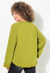 Haut vert olive à manches longues avec une coupe décontractée et des manches à poignets. Il présente un ourlet arrondi et des coutures visibles le long des coutures.