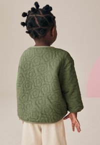 Vadderad, olivgrön sweatshirt med blommönster, rund halsringning och mjuk textur. Beiga ribbade byxor fulländar outfiten.