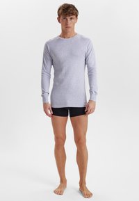 Lys grå langærmet skjorte i et blødt stof, med rund halsudskæring og figursyet silhuet, parret med sorte shorts.