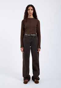 Brown ribbed knit long-sleeve top, high-waisted dark denim pants, studded black belt, and brown shoes. Smooth texture, relaxed fit.