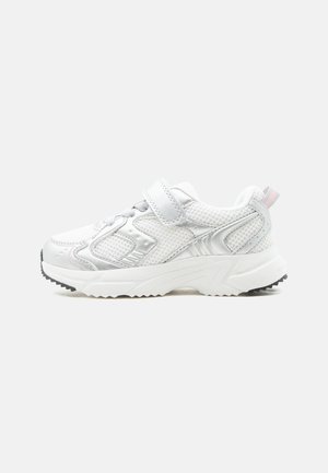 Baskets blanches sportives avec panneaux en mesh, bride Velcro, semelle épaisse et semelle noire sur fond neutre, vue de côté.