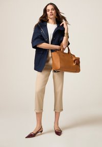 Navyblauwe waterdichte jas, crèmekleurige top, beige cropped broek en een bruine leren handtas. Burchundy lakleren slingbackschoenen met gouden accenten.