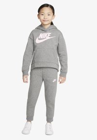Grå sweatshirt og matchende bukser laget av myk bomullsblanding, med en stor rosa Nike-logo på forsiden og siden av buksene.