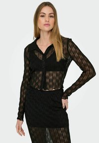 Sort gennemsigtig bluse med lange ærmer, knaplukning foran og tekstureret bølget design. Parret med en matchende sort nederdel, som begge har en flydende struktur.