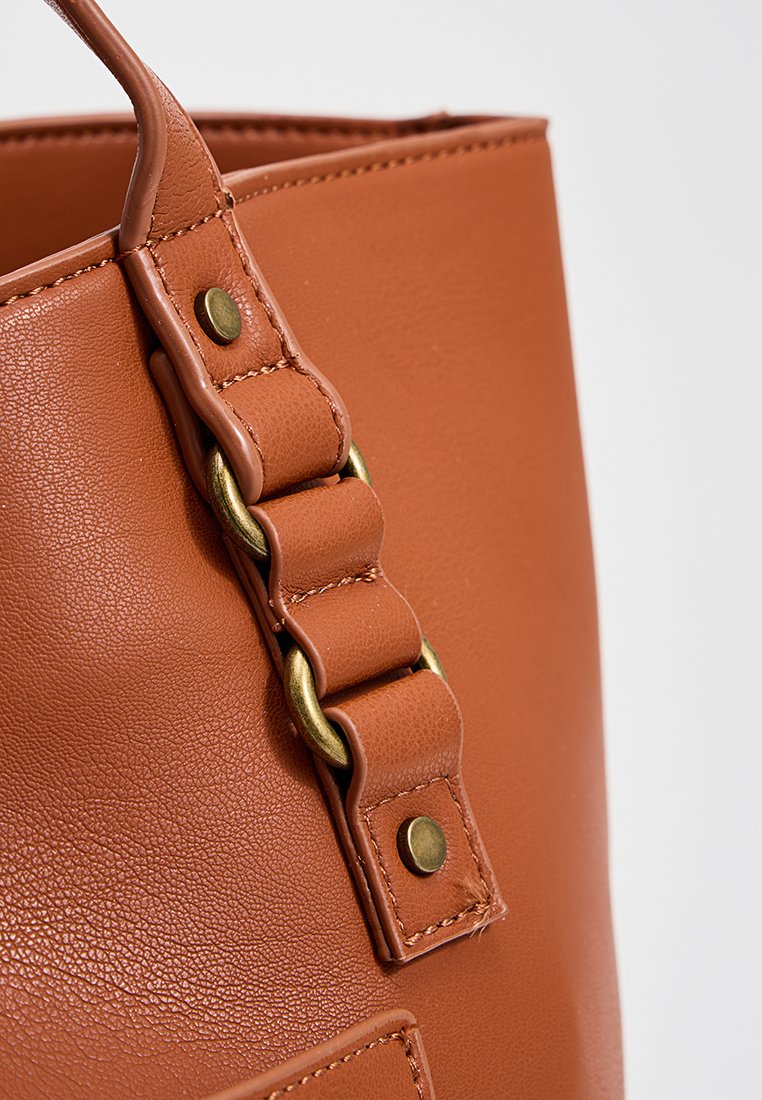 Bolso tote de piel marrón con una superficie texturizada. Cuenta con una correa gruesa con herrajes dorados y costuras decorativas a lo largo de los bordes.