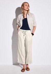 Lättvikts linneskjorta i beige, bärs ovanpå en marinblå linne-top; avslappnade krämfärgade vida byxor med justerbar dragsnodd. Bruna sandaler.