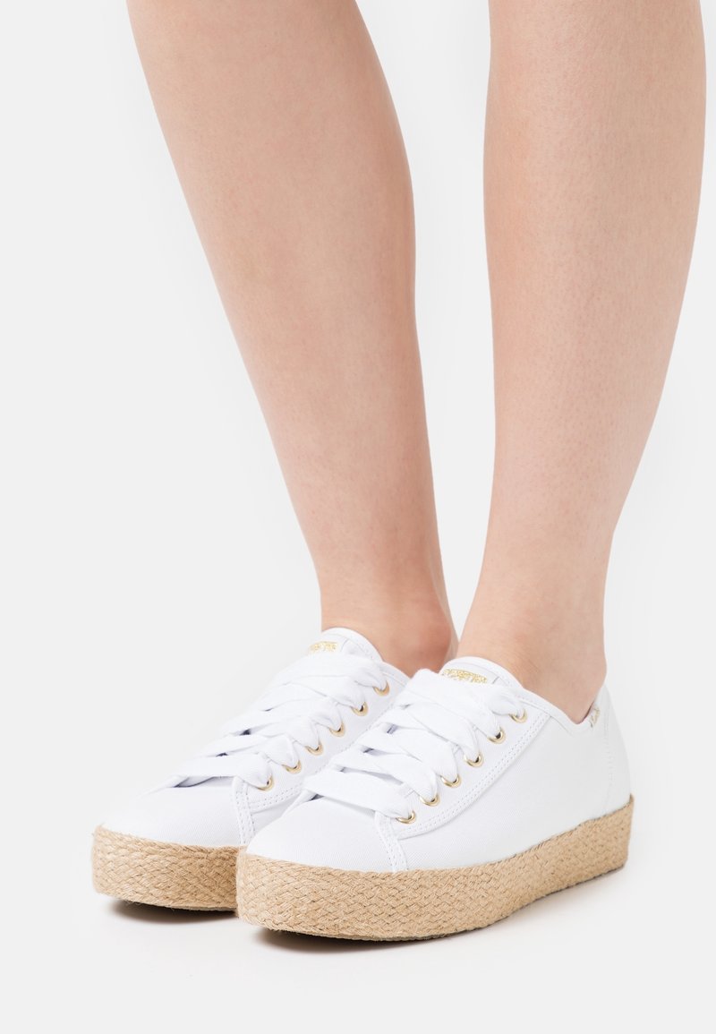 Sneakers bianche in tela con suola in corda di juta, caratterizzate da occhielli dorati, lacci e design con punta rotonda. Tessitura liscia e stile minimalista.