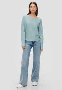 Hellblaues, geripptes Strickoberteil mit schulterfreier Ausschnittform, kombiniert mit weit geschnittenen hellblauen Jeans und weißen Plateausneakern.