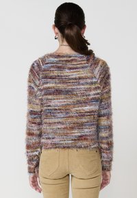 Bunt gemusterter, flauschiger Pullover mit horizontalen Streifen in burgunderrot, blau und gelb. Hat lange Ärmel und einen Rundhalsausschnitt.