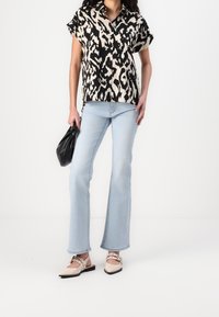 Chemise à manches courtes noir et crème à motifs, jean évasé bleu clair, ballerines beiges avec des brides à la cheville et un sac à main noir.