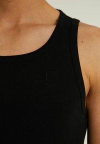 Čierny bezrukávový top vyrobený z hladkej látky, s okrúhlym výstrihom a malým vyšitým logom v ľavom hornom rohu.