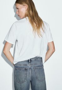 T-shirt bianco a maniche corte abbinato a jeans a vita alta blu sbiaditi. Tessuto liscio, taglio classico e dettagli di design minimi.