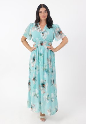 Robe maxi florale en tissu bleu clair. Comprend des manches bouffantes, une taille smockée et de grands motifs de fleurs blanches et vertes sur toute la surface.