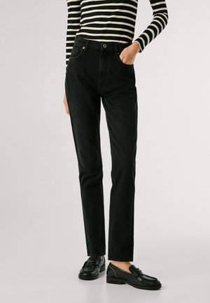 Person iført højtaljede, lige sorte jeans med hånden i lommen, kombineret med sorte teksturerede loafers og en sort og hvid stribet langærmet skjorte.