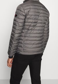 Veste rembourrée grise avec col montant, présentant des coutures horizontales, des poignets élastiques et un ourlet avec cordon de serrage ajustable.