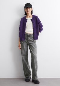 Cardigan lavorato a maglia viola con vestibilità ampia e bottoni, top bianco aderente, jeans grigi a gamba larga e scarpe platform nere chunky.