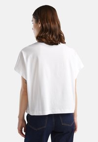 T-shirt bianco a maniche corte con vestibilità rilassata, caratterizzato da un colletto rotondo e spalle leggermente scese. Il tessuto è cotone morbido.