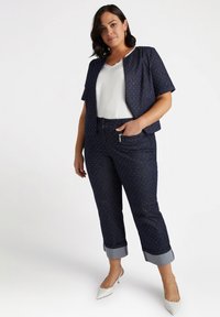 Mörk jeanjacka med korta ärmar, prydd med små vita prickar, i kombination med matchande jeans och en vit topp; har vikta manschetter.
