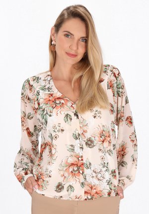Blusa floreale in morbido tessuto pesco chiaro, con grandi fiori arancioni e verdi, bottoni frontali e maniche lunghe con taglio rilassato.