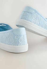 Baskets bleu clair à enfiler avec semelles en caoutchouc blanches et motifs floraux en tissu texturé sur les côtés.