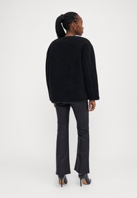 Čierny, veľký fleece sveter s dlhým rukávom a okrúhlym výstrihom, spárovaný s priliehavými čiernymi nohavicami a čiernymi vysokými podpätkami.