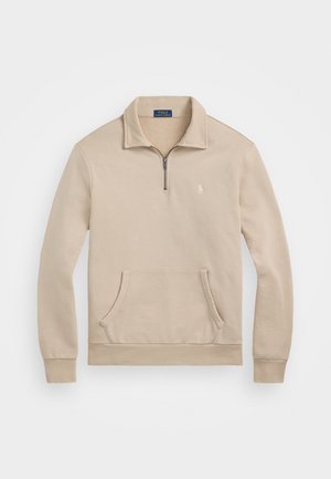 Beige genser med kvart glidelås, ribbestrikkede mansjetter, lomme foran, og en liten logo på brystet. Mykt, fleece-lignende materiale.
