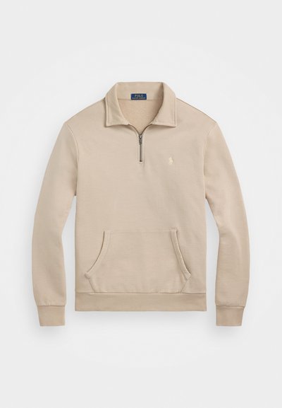 Sweatshirt bege com gola de fecho de correr de um quarto, punhos canelados, bolso frontal e um pequeno logótipo no peito. Material macio, semelhante a tecido polar.