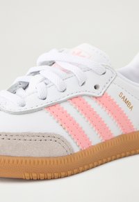 White sneaker with pink three stripes and 'Samba' label, featuring a textured gray suede toe cap and a gum rubber sole.