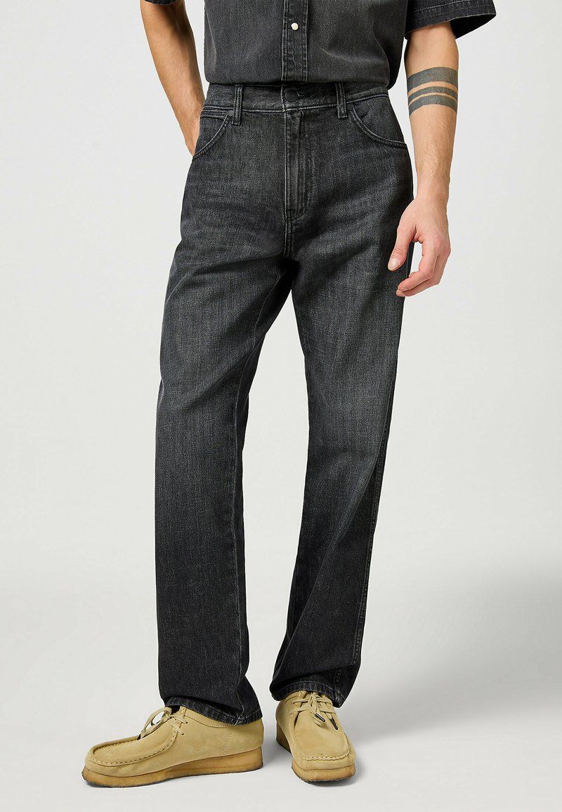 Pantalones vaqueros de mezclilla negra con un diseño de pierna recta, con una cintura alta, cinco bolsillos y detalles de costura sutiles, combinados con zapatos de mocasín beige.