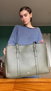 Saco tote de couro verde com duas alças, superfície texturizada e um logotipo subtil na parte inferior. Apresenta um design espaçoso.