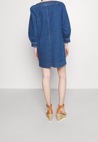 Abito in denim con una vestibilità ampia, maniche a sbuffo e taglio dritto. Colore azzurro chiaro, cuciture a contrasto, con un orlo poco sopra le ginocchia.