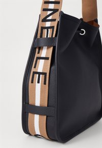 Borsa in pelle nera con finitura texturizzata, dotata di una tracolla intrecciata beige con lettere nere e strisce bianche, vista angolata che mostra il bordo superiore.
