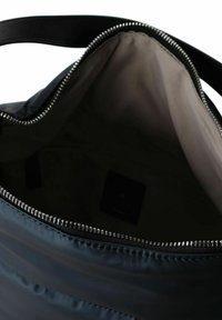 Bolso acolchado azul marino con una textura suave, cierre superior con cremallera y una correa de cuero negro. El interior presenta un forro claro y visibilidad de la etiqueta.