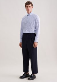Camicia a righe azzurro chiaro con bottoni, pantaloni plissettati blu scuro e scarpe di pelle nere. Design semplice e vestibilità su misura, tessuto dalla trama liscia.