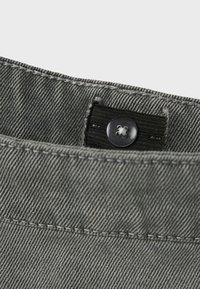 Grau denim Taillenbund mit einem schwarzen Gummiband, ausgestattet mit einem runden Kunststoffknopf und kontrastierenden weißen Nähten für eine detaillierte Textur.