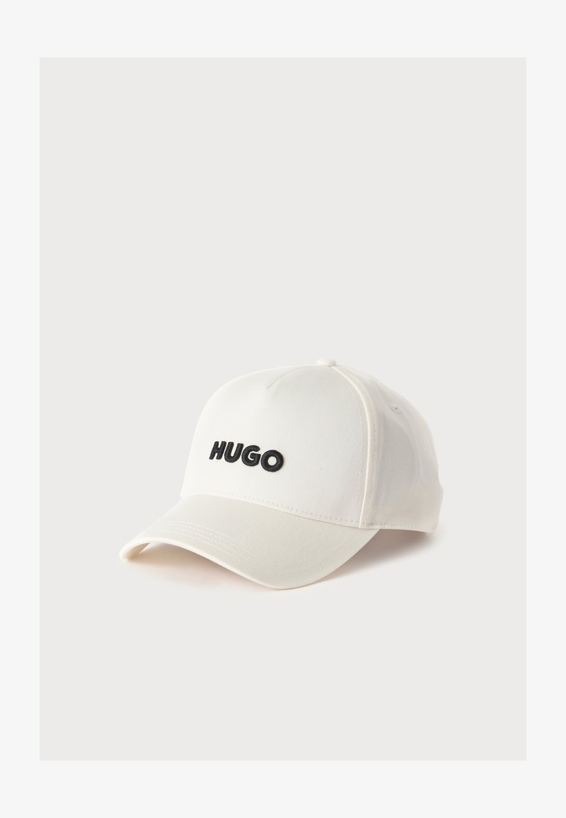 Casquette de baseball blanche avec une visière incurvée et "HUGO" brodé en noir sur le devant sur un fond clair uni.