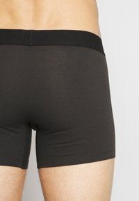 Bóxers de algodón negro con un diseño liso, cinta elástica de altura media y sin patrones visibles ni detalles metálicos.