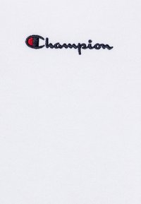 Tessuto di cotone bianco con un logo "Champion" ricamato in blu con un accento rosso, progettato in uno stile classico e informale.